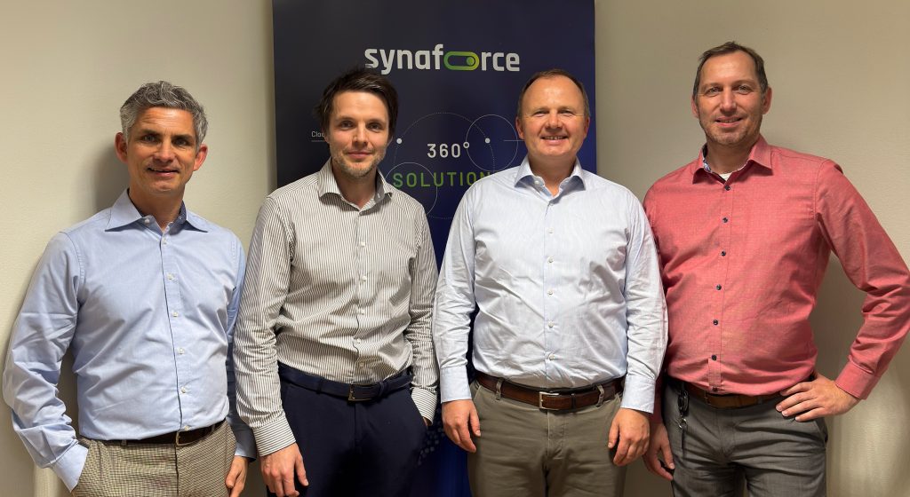 Vier Synaforce-Führungskräfte stehen zusammen vor einem Firmenbanner im Headquarter in Hofkirch.